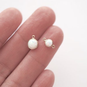 May include: Two gold-toned metal charms with white opal-like stones. One charm has a loop for attaching to a chain or bracelet, while the other has a jump ring.