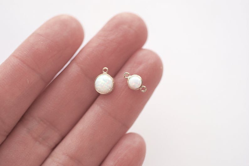 May include: Two gold-toned metal charms with white opal-like stones. One charm has a loop for attaching to a chain or bracelet, while the other has a jump ring.