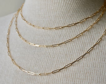 Könnte beinhalten: Drei goldene Kettenhalsbänder mit einem Gliederketten-Design. Die Ketten sind auf einem weißen Mannequin übereinander gelegt.