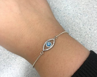 Puede incluir: Una pulsera de plata con un dije de ojo turco azul rodeado de brillantes transparentes.