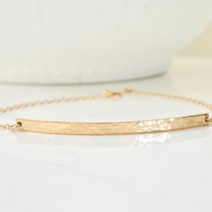 May include: A delicate gold bracelet with a hammered bar pendant. The chain is a simple, delicate chain.