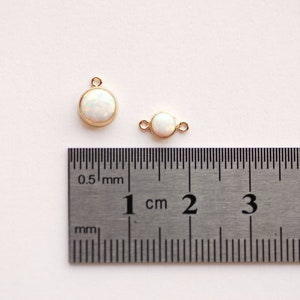 May include: Two gold-toned charms with white opal stones. The larger charm is 1 cm in diameter and the smaller charm is 0.5 cm in diameter.