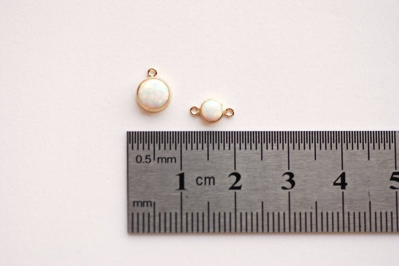 May include: Two gold-toned charms with white opal stones. The larger charm is 1 cm in diameter and the smaller charm is 0.5 cm in diameter.