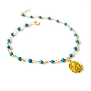 May include: A gold chain necklace with turquoise beads and a gold angel pendant.