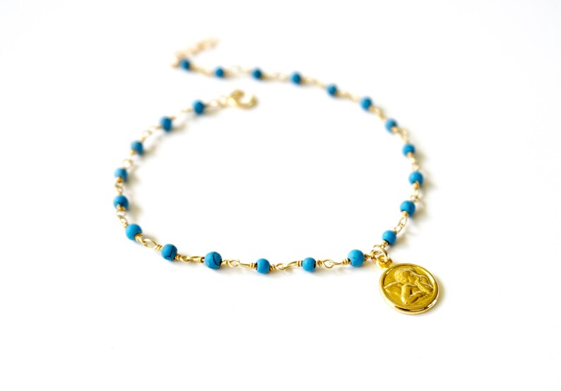 May include: A gold chain necklace with turquoise beads and a gold angel pendant.
