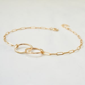 May include: A gold chain bracelet with two interlocking circles. The chain is made of small, linked ovals.