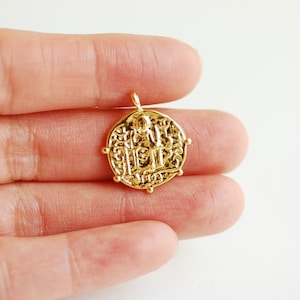 May include: Gold pendant necklace featuring a round coin charm with an intricate design. The coin has a raised center with a figure and ornate details.