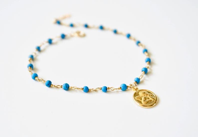 May include: A gold chain necklace with turquoise blue beads and a gold angel pendant.