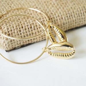 May include: Gold hoop earrings with a seashell charm. The earrings are simple and elegant, perfect for everyday wear.