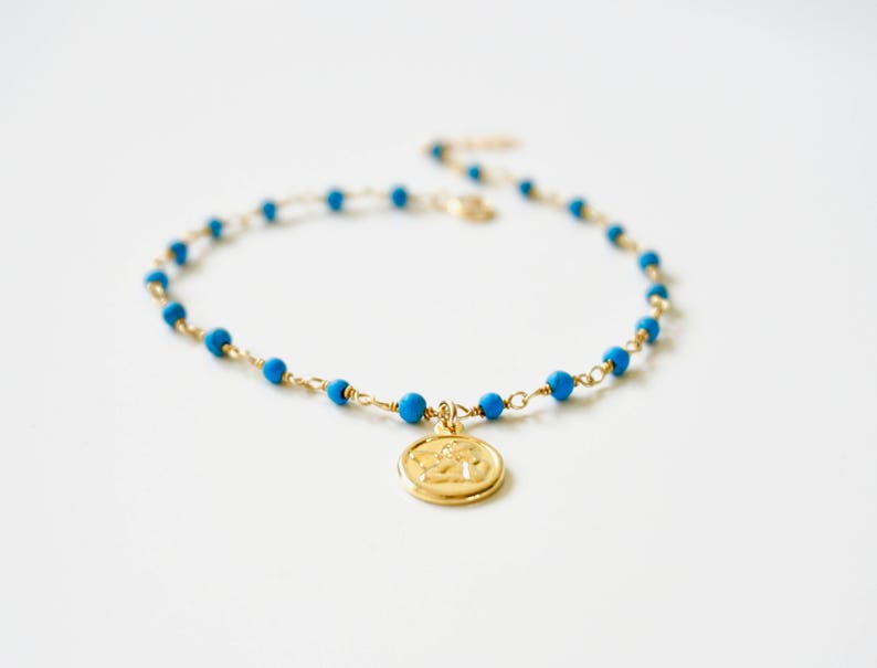 May include: A gold chain bracelet with blue beads and a gold charm. The charm is a round disc with a design on it.