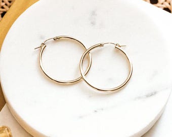 May include: A pair of gold hoop earrings on a white marble surface.