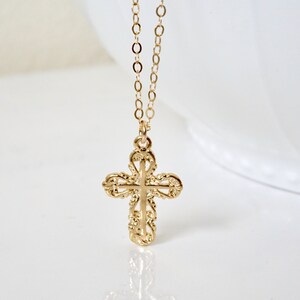 May include: A gold chain necklace with a delicate, ornate cross pendant. The cross is detailed with intricate scrollwork and has a slightly raised center.
