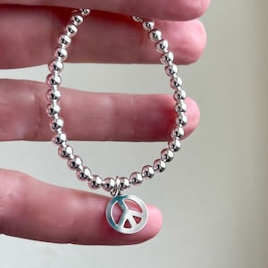 May include: A silver beaded bracelet with a peace sign charm.
