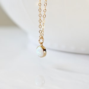 May include: A delicate gold chain necklace with a small, round white opal pendant.