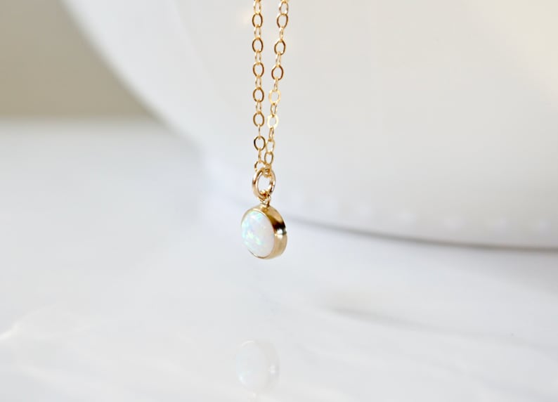 May include: A delicate gold chain necklace with a small, round white opal pendant.