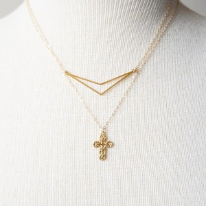May include: A gold necklace with a delicate cross pendant and a geometric chevron design. The necklace is layered on a white mannequin.