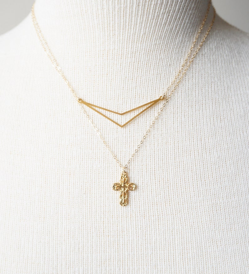 May include: A gold necklace with a delicate cross pendant and a geometric chevron design. The necklace is layered on a white mannequin.