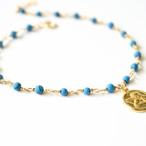 May include: A gold chain necklace with blue beads and a gold pendant featuring an angel design.