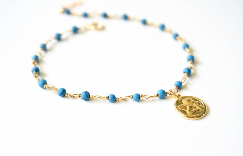 May include: A gold chain necklace with blue beads and a gold pendant featuring an angel design.