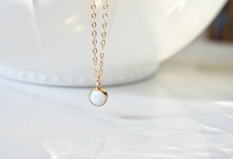 May include: A delicate gold chain necklace with a small, round white opal pendant.