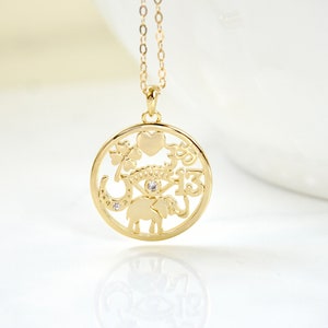 May include: Gold-toned pendant necklace with a circular charm. The charm features cut-out designs of a heart, four-leaf clover, horseshoe, eye, elephant, and the number 13. A small, clear gem is set in the center of the eye.
