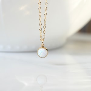 May include: A delicate gold chain necklace with a small, round white opal pendant.
