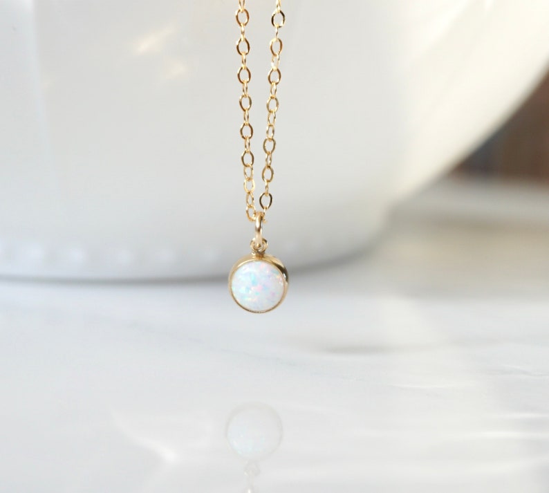 May include: A delicate gold chain necklace with a small, round white opal pendant.