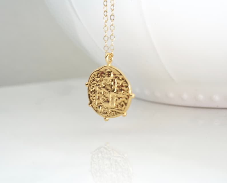 May include: Gold necklace with a coin pendant featuring an intricate design. The coin is oval-shaped and has a textured surface.