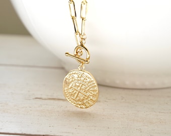 May include: Gold chain necklace with a large, round, textured coin pendant. The chain has a toggle clasp.