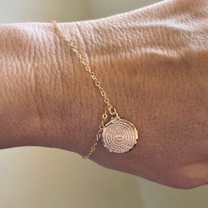 Puede incluir: Un brazalete de cadena dorada con un colgante circular que presenta un diseño en espiral detallado.
