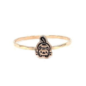 May include: A gold ring with a hammered finish and a small cat charm. The cat charm is black and white and has a cute expression.