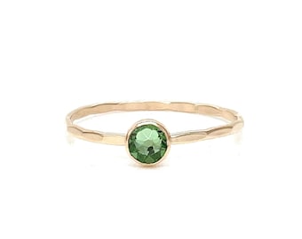 May include: A delicate gold ring with a hammered band and a round green gemstone.
