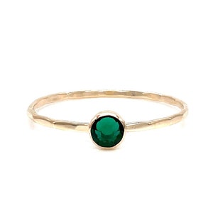 May include: A delicate gold ring with a hammered band and a single round emerald green gemstone.