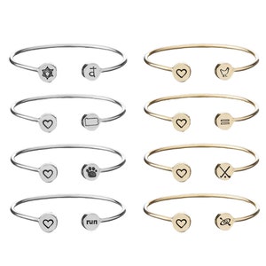 May include: Eight silver and gold bangle bracelets with different engraved symbols and words. The symbols include a heart, a star of David, a cross, a paw print, a bird, an equal sign, a crossbones, and a compass. The words include "run" and "love".