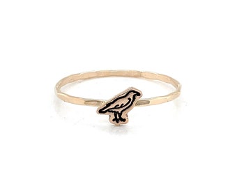 May include: A gold-colored ring featuring a black and gold bird design. The ring has a thin band and a small, detailed bird silhouette. The bird is depicted in a standing position, with its wings and body clearly defined.