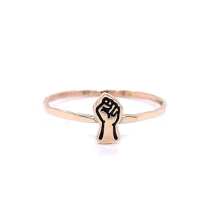 May include: A gold ring with a raised black fist design.