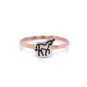 Pode incluir: Um anel de ouro rosa com uma banda martelada e um berloque de unicórnio prateado. O unicórnio é delineado em preto e fica sobre uma base prateada. Uma joia simples e elegante.