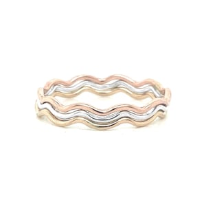 May include: Three thin wavy bands, one gold, one silver, and one rose gold, are stacked together to form a ring.