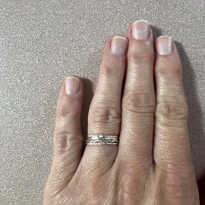 May include: A close-up of a hand wearing a silver ring with a textured design. The ring is worn on the ring finger of the right hand.