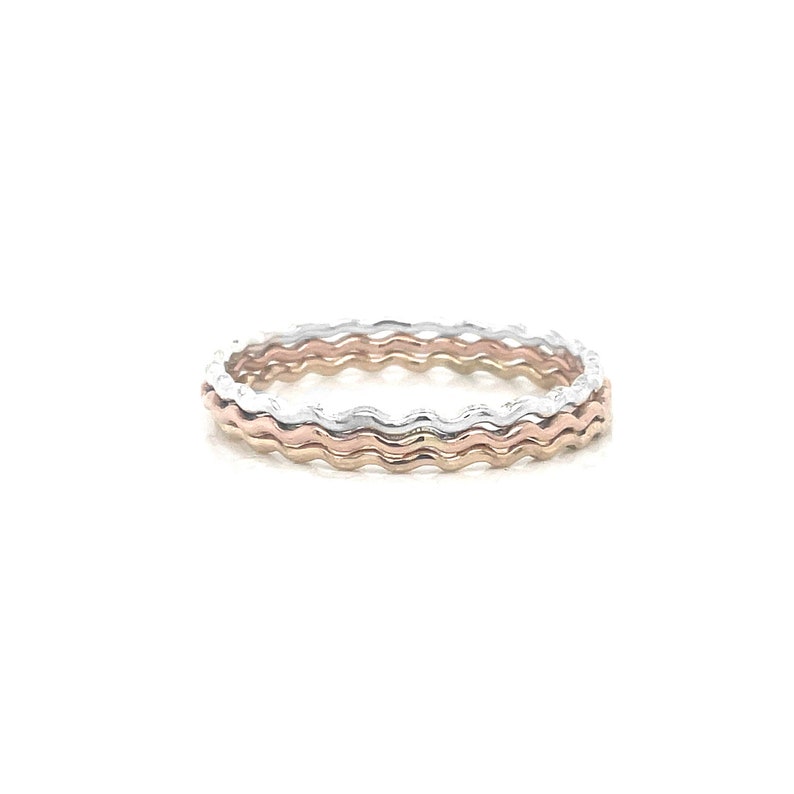 May include: Three thin wave-shaped rings stacked together. The top ring is silver, the middle ring is rose gold, and the bottom ring is silver.