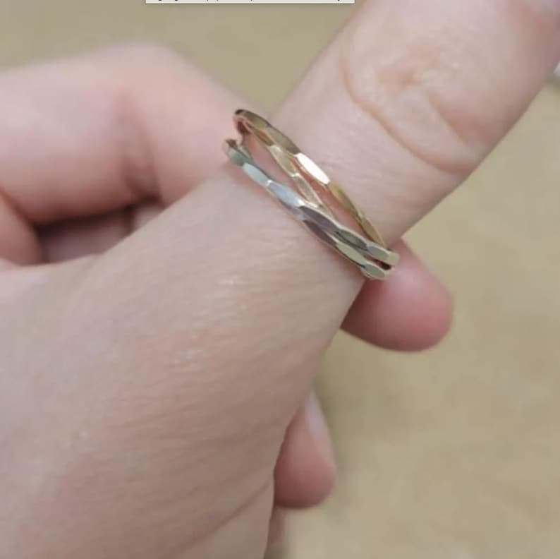K&ouml;nnte beinhalten: Nahaufnahme von zwei Ringen, einem goldenen und einem silbernen, die auf einem Finger gestapelt sind. Die Ringe haben ein strukturiertes, facettiertes Design, das das Licht einf&auml;ngt. Der goldene Ring liegt &uuml;ber dem silbernen Ring.