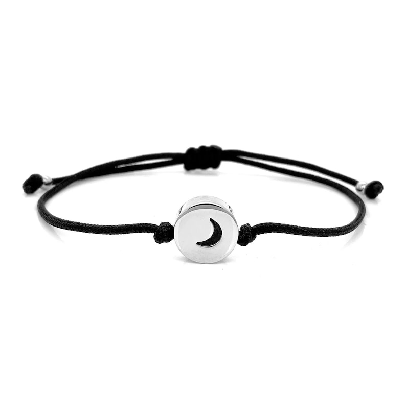 May include: A black string bracelet with a silver charm featuring a crescent moon design.