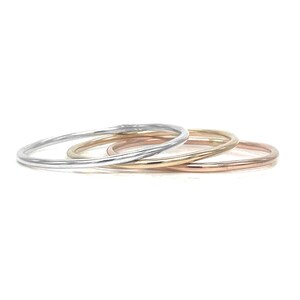 May include: Three thin stacking rings in silver, gold, and rose gold.