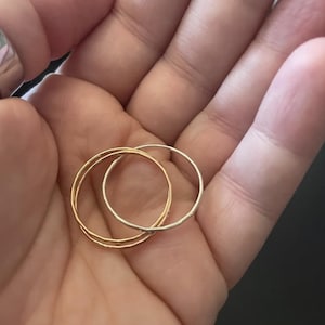 K&ouml;nnte beinhalten: Nahaufnahme von drei d&uuml;nnen Ringen: zwei goldfarben und einer silberfarben. Die Ringe sind &uuml;bereinander gestapelt, wodurch ein geschichteter Effekt entsteht. Die goldenen Ringe haben eine strukturierte Oberfl&auml;che, w&auml;hrend der silberne Ring glatt erscheint. Die Ringe werden in einer Hand gehalten.