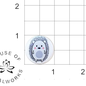 May include: A white button with a cute cartoon hedgehog with pink cheeks and a gray body. The hedgehog is surrounded by a black outline and a white background.