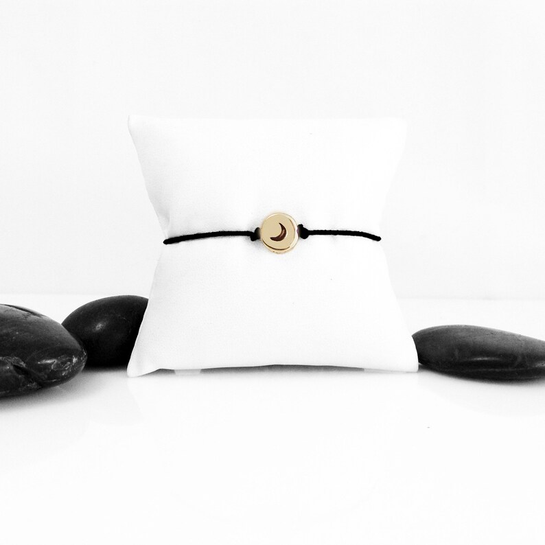 May include: A black string bracelet with a gold charm featuring a crescent moon design.
