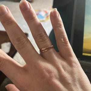K&ouml;nnte beinhalten: Ein ros&eacute;goldener Ring an einem Finger. Der Ring hat ein minimalistisches Design mit zwei d&uuml;nnen B&auml;ndern. Die B&auml;nder sind durch kleine, rechteckige Akzente verbunden. Der Ring ist ein schlichtes, aber elegantes Schmuckst&uuml;ck.