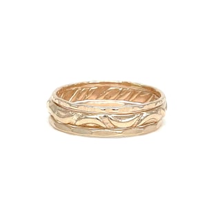 May include: Three gold stacking rings with different textures. The top ring has a wavy pattern, the middle ring has a hammered texture, and the bottom ring has a smooth finish.