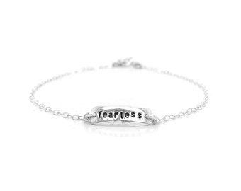 May include: A silver chain bracelet with a rectangular charm that says "fearless" in black lettering.