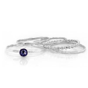 May include: Set of four silver stacking rings, one with a small purple gemstone. The rings are all hammered and have a textured finish.